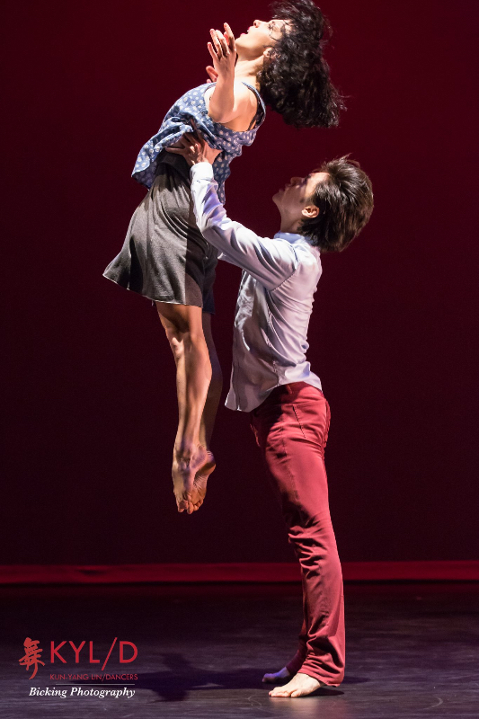 Liu Mo in red jean jeans lifts Evalina Carbonelli from her rib cage. Carbonell arches back and points her feet underneath her